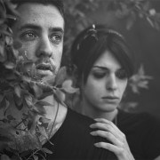 Black and white photo of couple standing in bushes, looking hopelessly into the distance.