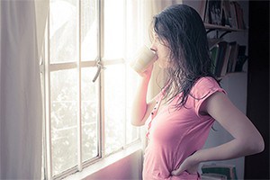 Woman drinking a cup of coffee, looking thoughtfully out a window. 