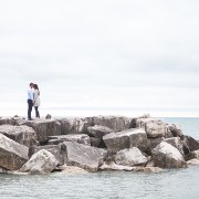 Couple standing on rocks over water.