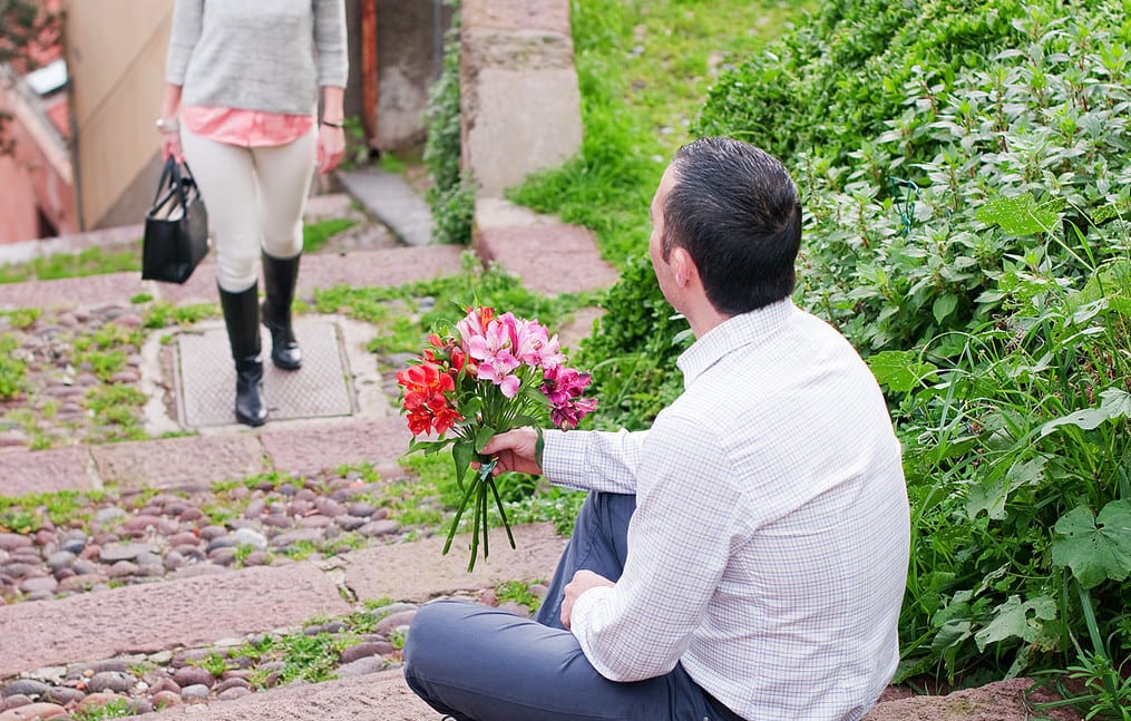 man waiting on steps for woman with flowers 